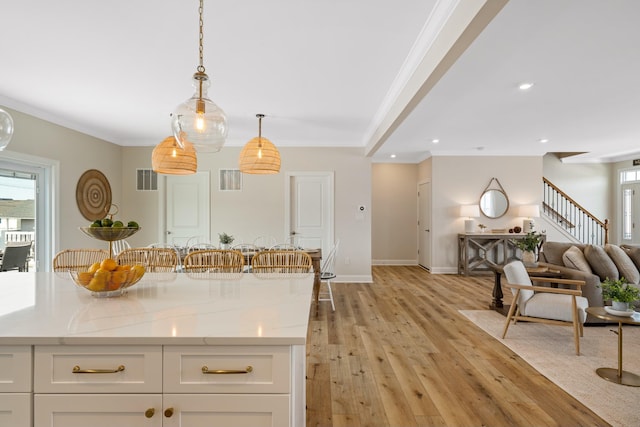 kitchen featuring light stone countertops, ornamental molding, pendant lighting, light hardwood / wood-style floors, and white cabinetry