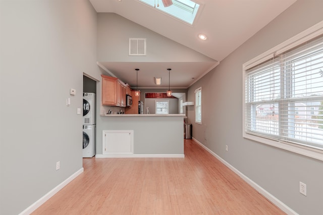 kitchen with hanging light fixtures, a skylight, stainless steel appliances, stacked washer and clothes dryer, and light hardwood / wood-style floors