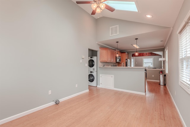 interior space featuring ceiling fan, stacked washing maching and dryer, hanging light fixtures, stainless steel appliances, and light wood-type flooring