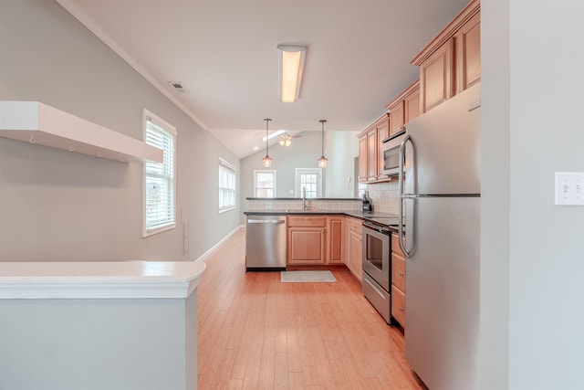 kitchen featuring vaulted ceiling, appliances with stainless steel finishes, hanging light fixtures, kitchen peninsula, and light brown cabinets