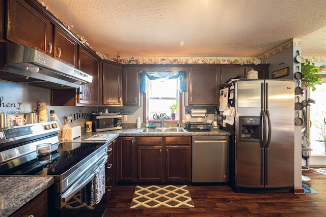 kitchen with appliances with stainless steel finishes, dark hardwood / wood-style flooring, a textured ceiling, dark brown cabinetry, and sink