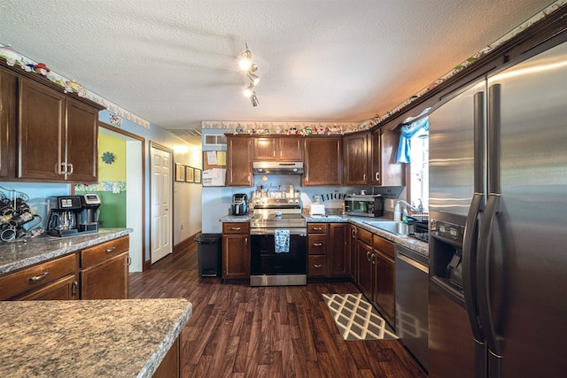 kitchen with dark wood-type flooring, sink, light stone countertops, a textured ceiling, and stainless steel appliances