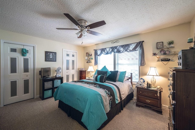 carpeted bedroom featuring multiple closets, ceiling fan, and a textured ceiling