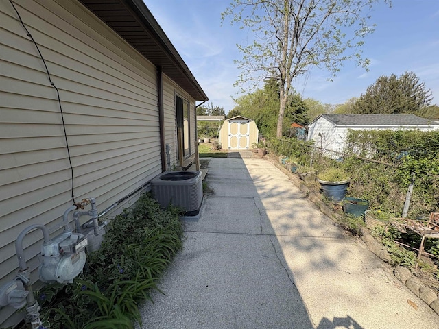 view of side of home featuring a storage unit, an outbuilding, cooling unit, fence, and a patio
