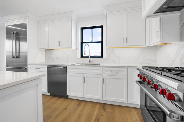 kitchen featuring high quality appliances, premium range hood, white cabinets, light wood-type flooring, and light stone counters