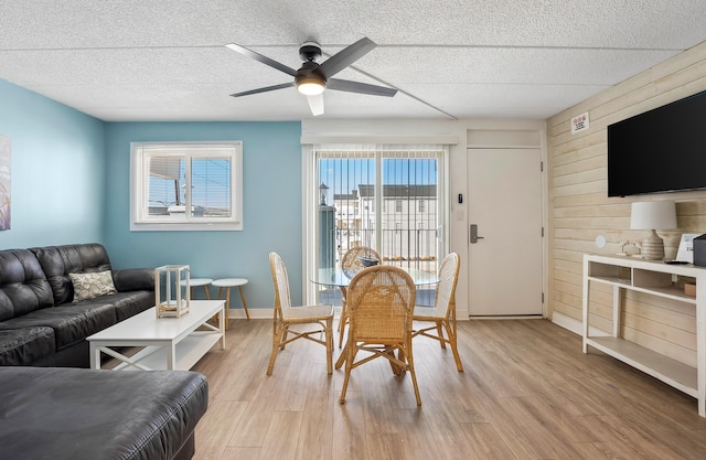 dining area featuring baseboards, a ceiling fan, a textured ceiling, light wood-type flooring, and wood walls