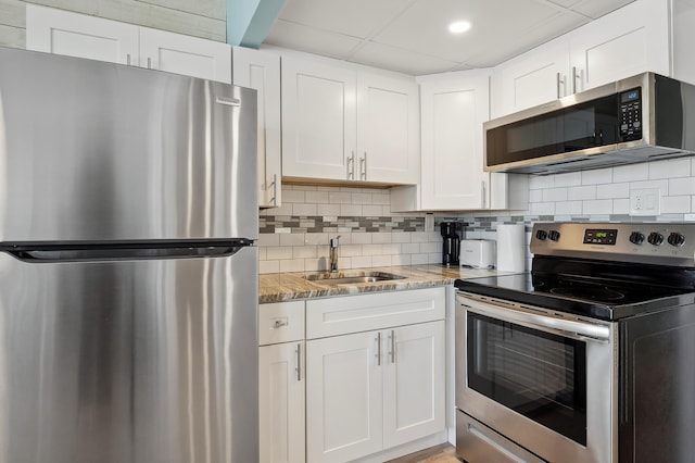 kitchen featuring stainless steel appliances, white cabinetry, a sink, and decorative backsplash