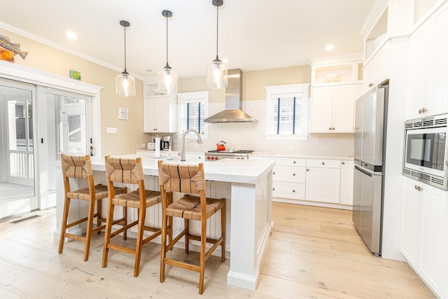 kitchen featuring pendant lighting, a kitchen breakfast bar, stainless steel appliances, an island with sink, and wall chimney exhaust hood