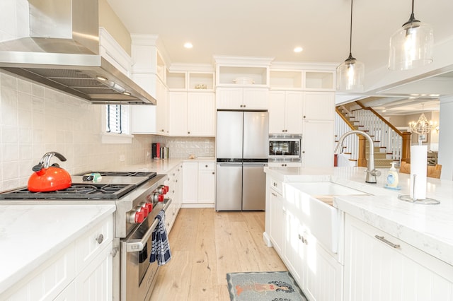 kitchen with appliances with stainless steel finishes, wall chimney range hood, white cabinets, and decorative light fixtures