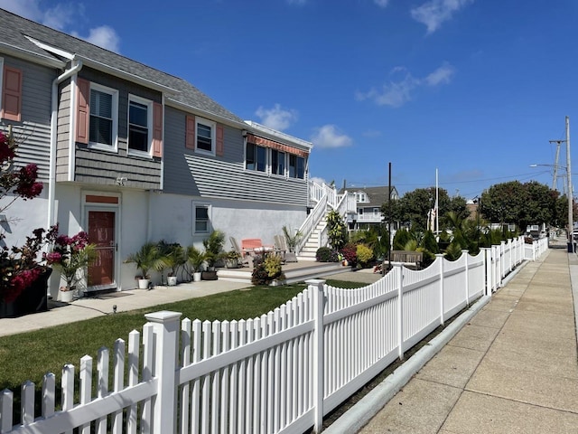 435 W Pine Ave, Wildwood, NJ 08260 - view of home's exterior featuring a fenced front yard, stairs, roof with shingles, and stucco siding