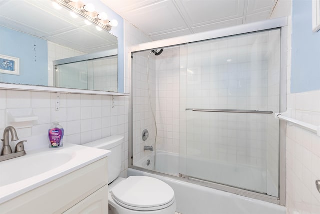 full bath featuring toilet, shower / bath combination with glass door, vanity, and tile walls