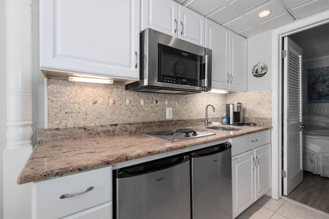 kitchen featuring light tile patterned floors, stainless steel appliances, a sink, white cabinets, and tasteful backsplash