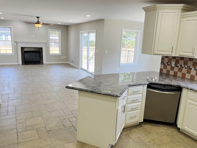 kitchen with kitchen peninsula, tasteful backsplash, a healthy amount of sunlight, dark stone countertops, and dishwasher