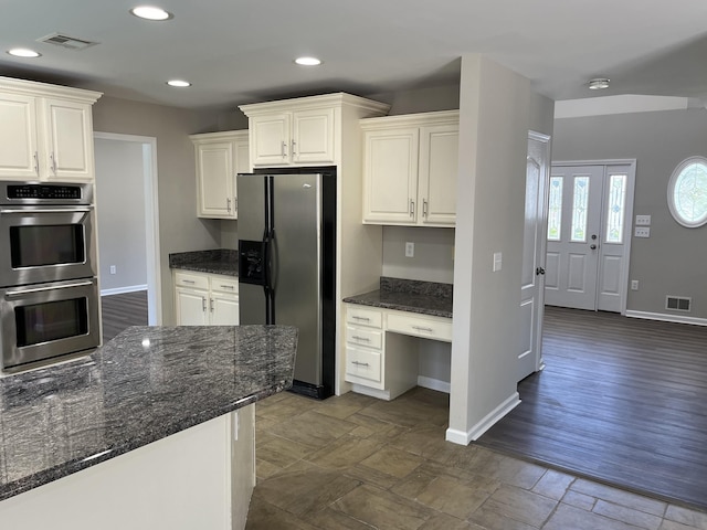 kitchen with dark stone countertops, white cabinetry, appliances with stainless steel finishes, and built in desk