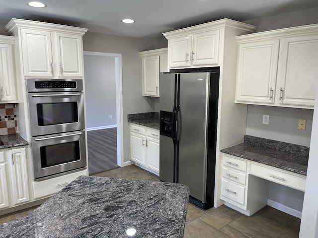 kitchen with white cabinetry, dark stone countertops, built in desk, and stainless steel appliances