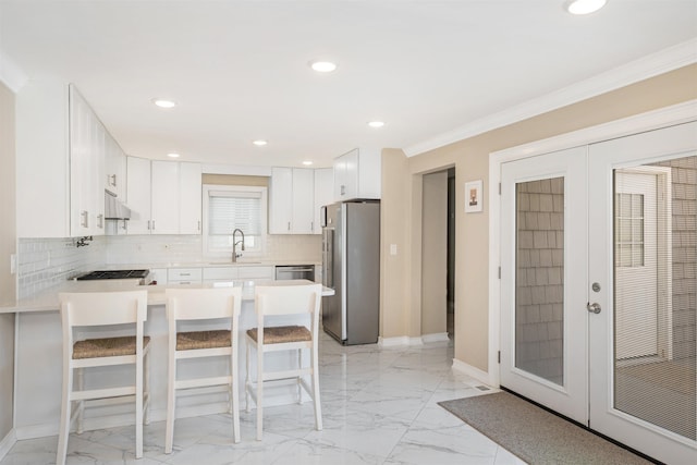 kitchen featuring backsplash, white cabinets, appliances with stainless steel finishes, a kitchen bar, and kitchen peninsula