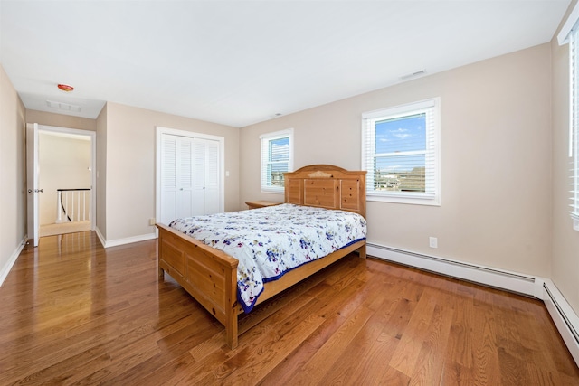 bedroom featuring wood-type flooring, baseboard heating, and a closet