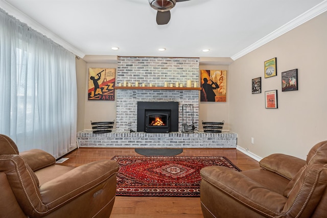 living room featuring ceiling fan, hardwood / wood-style floors, ornamental molding, and a brick fireplace