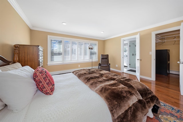 bedroom with baseboard heating, crown molding, hardwood / wood-style flooring, a spacious closet, and a closet