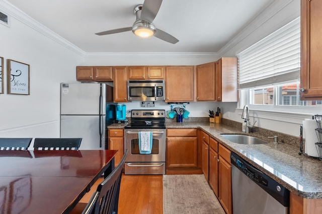 kitchen featuring appliances with stainless steel finishes, ornamental molding, a sink, brown cabinetry, and light wood finished floors