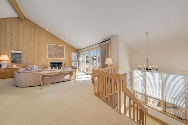 carpeted living area featuring wooden walls, a chandelier, beam ceiling, a glass covered fireplace, and high vaulted ceiling