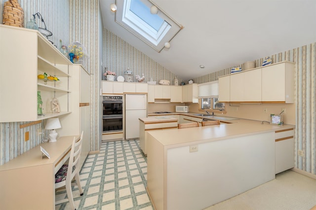 kitchen with wallpapered walls, light countertops, a skylight, white appliances, and a sink