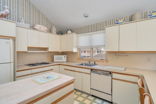 kitchen with white appliances, light floors, wallpapered walls, a sink, and light countertops