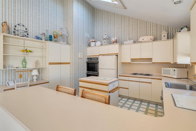 kitchen featuring a sink, wallpapered walls, white appliances, a skylight, and light countertops