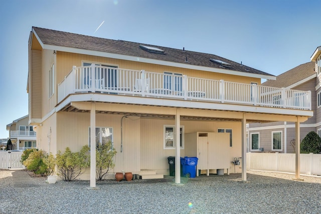 back of house with a shingled roof, a deck, and fence