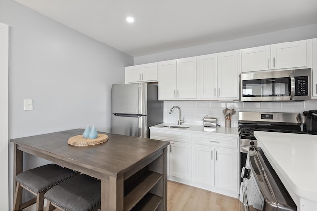 kitchen with sink, appliances with stainless steel finishes, white cabinetry, tasteful backsplash, and light wood-type flooring