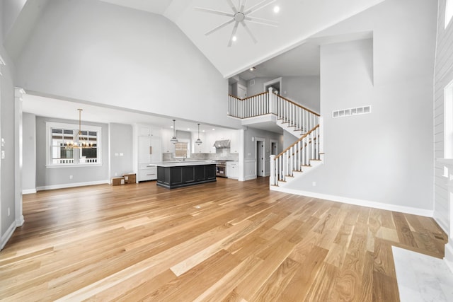 65 E 24th St, Avalon, NJ 08202 - unfurnished living room with high vaulted ceiling, light wood-type flooring, stairway, a chandelier, and ceiling fan