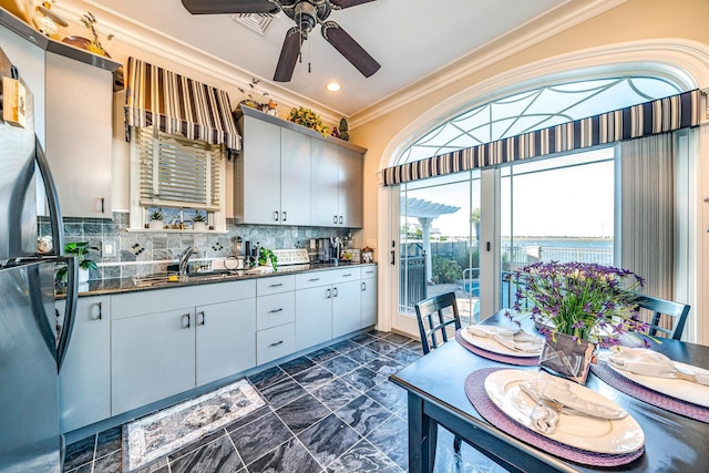 kitchen featuring ceiling fan, sink, stainless steel fridge, crown molding, and decorative backsplash