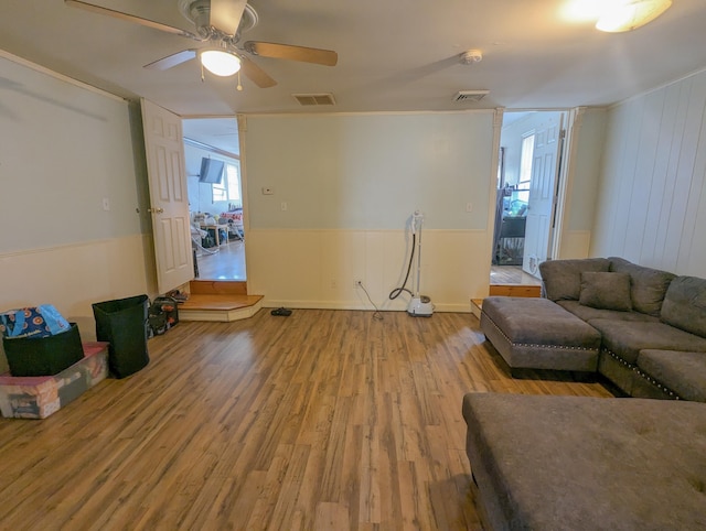 living area featuring visible vents, a wainscoted wall, wood finished floors, and a ceiling fan