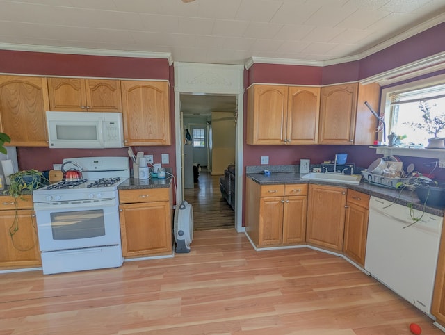 kitchen featuring white appliances, a sink, crown molding, light wood-style floors, and dark countertops