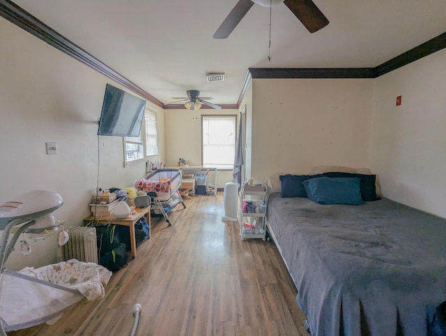 bedroom featuring visible vents, a ceiling fan, wood finished floors, radiator, and crown molding