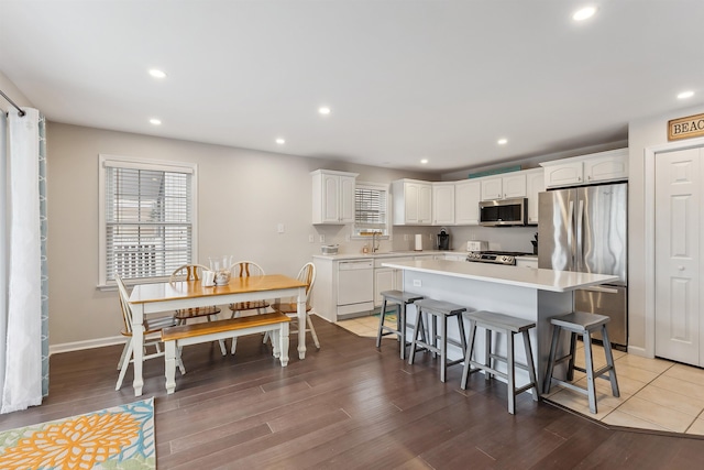 kitchen featuring stainless steel appliances, white cabinetry, a sink, a kitchen island, and a kitchen breakfast bar