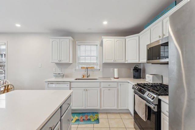 kitchen with appliances with stainless steel finishes, light tile patterned flooring, white cabinetry, a sink, and recessed lighting