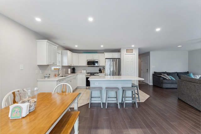 kitchen featuring appliances with stainless steel finishes, wood finished floors, a center island, white cabinetry, and a sink