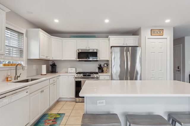 kitchen with light tile patterned floors, stainless steel appliances, white cabinetry, a sink, and a kitchen breakfast bar