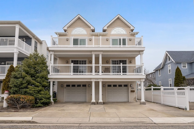 coastal home with concrete driveway, fence, a balcony, and an attached garage