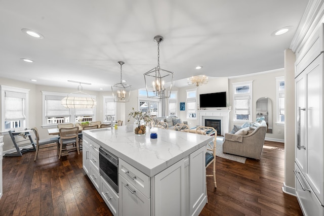 kitchen featuring white cabinets, open floor plan, light stone countertops, stainless steel microwave, and pendant lighting