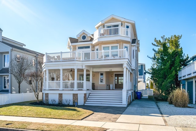 view of front of house with a ceiling fan, a balcony, covered porch, fence, and a front lawn