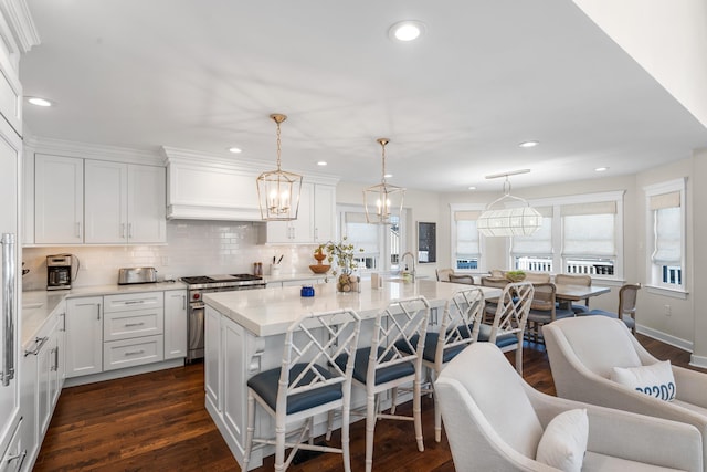 kitchen featuring white cabinets, stainless steel range, a kitchen island with sink, and pendant lighting