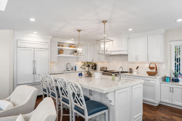 kitchen with light stone counters, white cabinetry, a kitchen island with sink, and pendant lighting