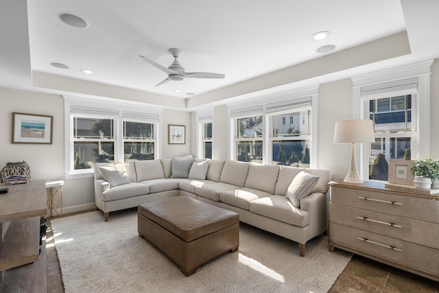 living area with ceiling fan, recessed lighting, a raised ceiling, and baseboards