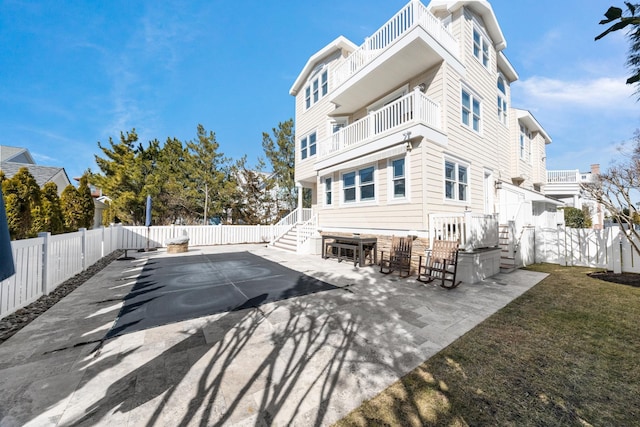 back of property featuring a balcony, a patio area, a fenced backyard, and a yard