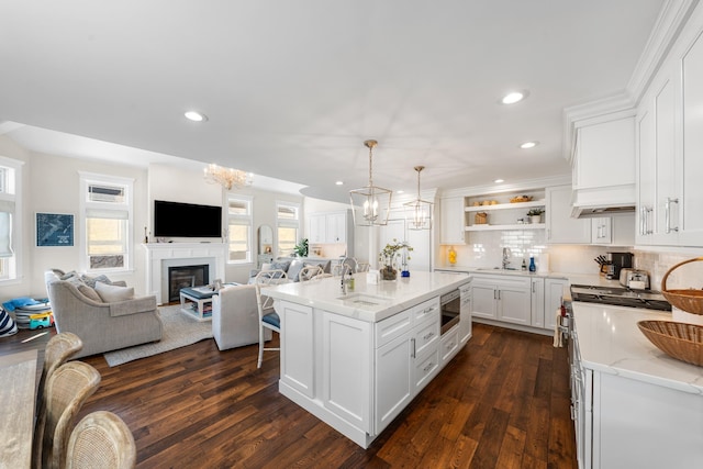 kitchen featuring light stone counters, decorative light fixtures, a center island with sink, stainless steel microwave, and white cabinets