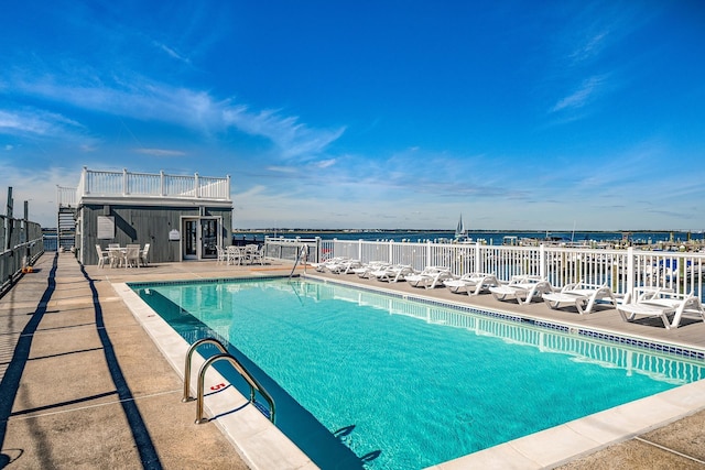 community pool featuring a water view, a patio area, and fence