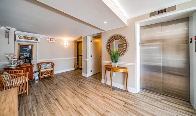 sitting room with elevator, light wood-style flooring, baseboards, and crown molding