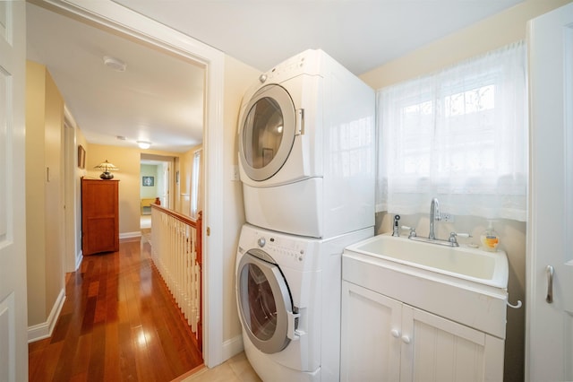 washroom with baseboards, a sink, light wood-style flooring, and stacked washing maching and dryer